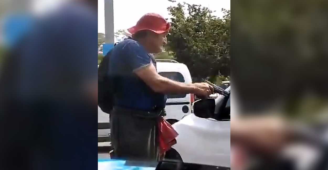 El hombre de tercera edad le apunta a los automovilistas para que le den dinero.